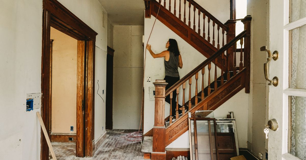 A woman working on home renovation featuring a wooden staircase.