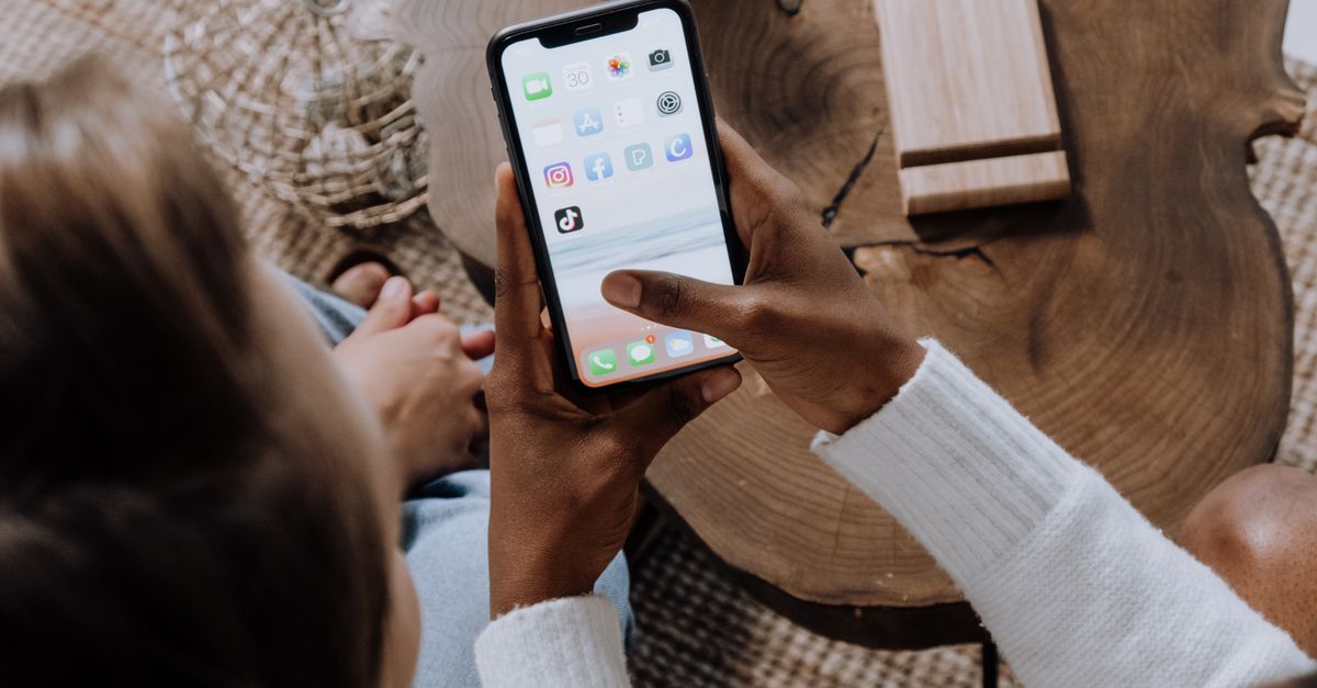 A person using a smartphone with social media apps, sitting at a wooden table. Perfect for tech lifestyle content.