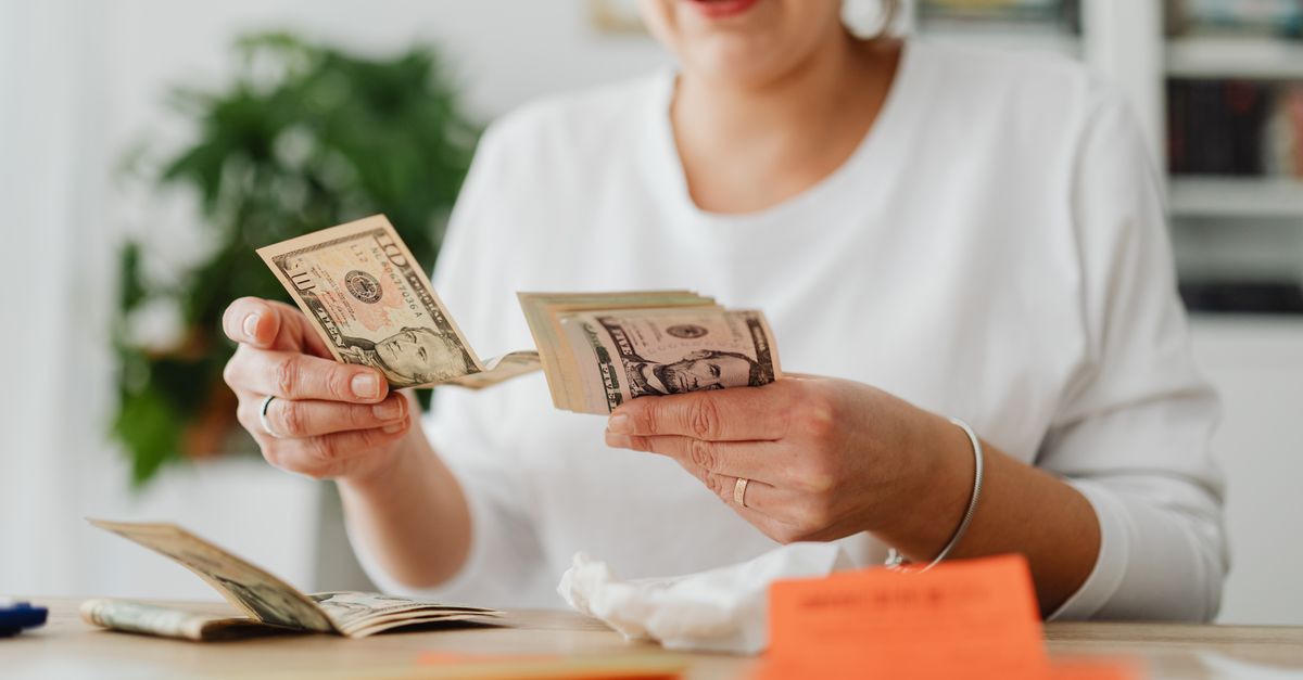 A woman sits indoors counting cash at her office desk, focusing on finances.